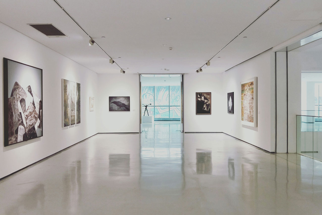 Interno di una galleria d'arte moderna, con opere esposte su pareti bianche, illuminazione uniforme e pavimento lucido.
