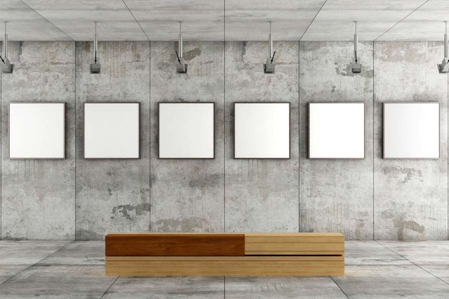 Interno di una galleria d'arte moderna con pareti in cemento, cinque telai bianchi vuoti appesi e una consolle in legno.